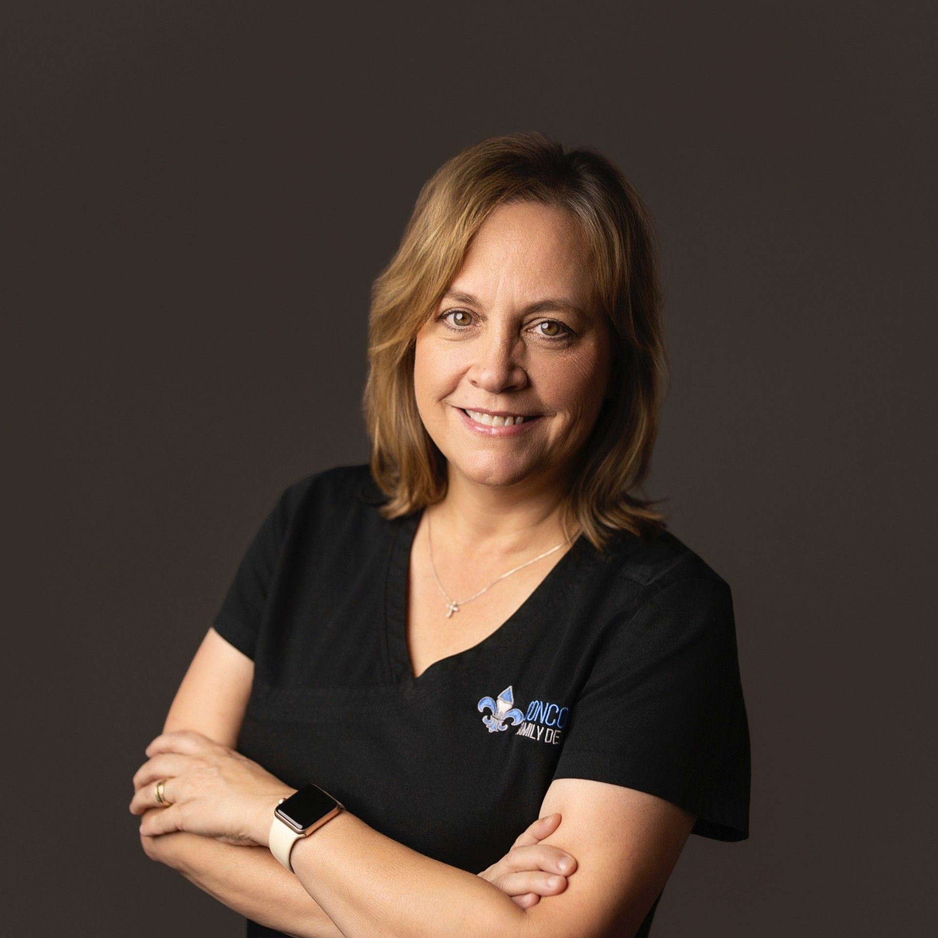 Woman with arms crossed, wearing black shirt with logo, smiling.