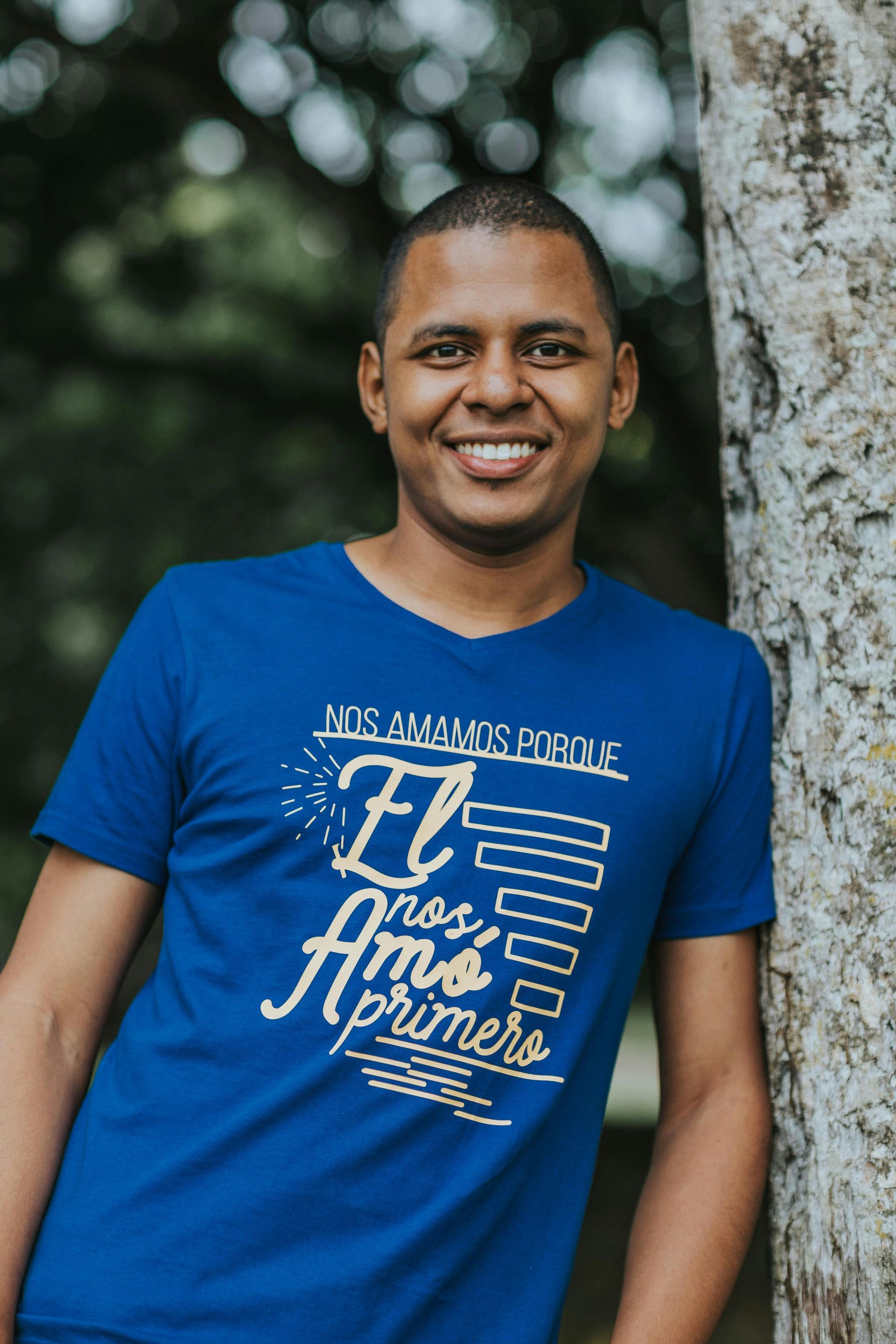 A man in a blue shirt is standing next to a tree.