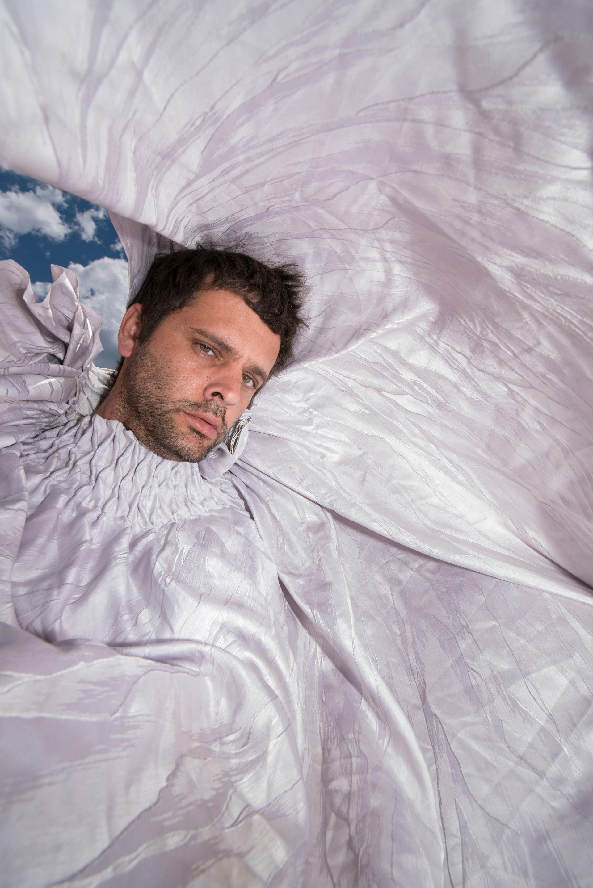 A man is laying on a white cloth with his head sticking out of it.