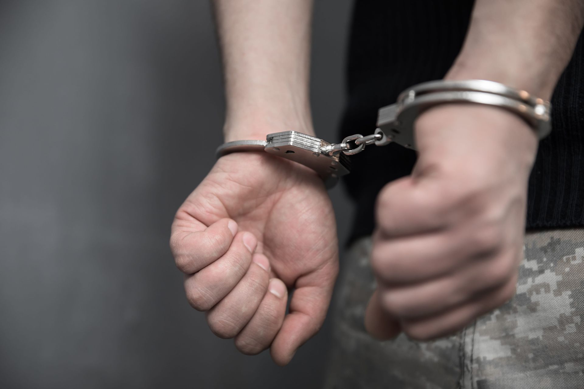 Handcuffed wrists held behind the back of a person in military-style clothing.