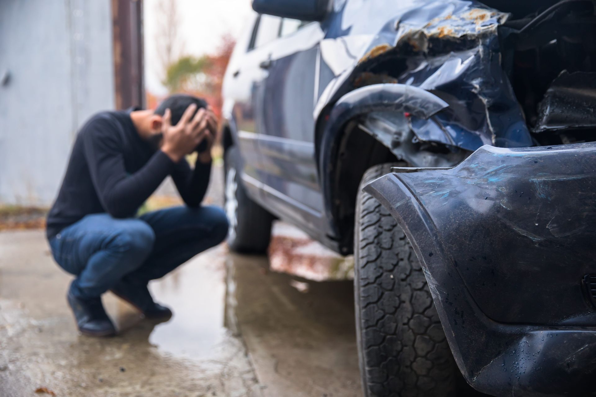 Person crouching beside a damaged car after a collision