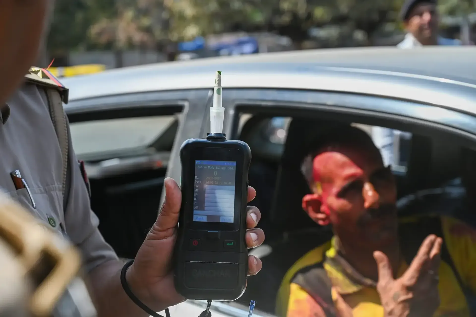 Officer holding a handheld breathalyzer beside a car with a driver inside