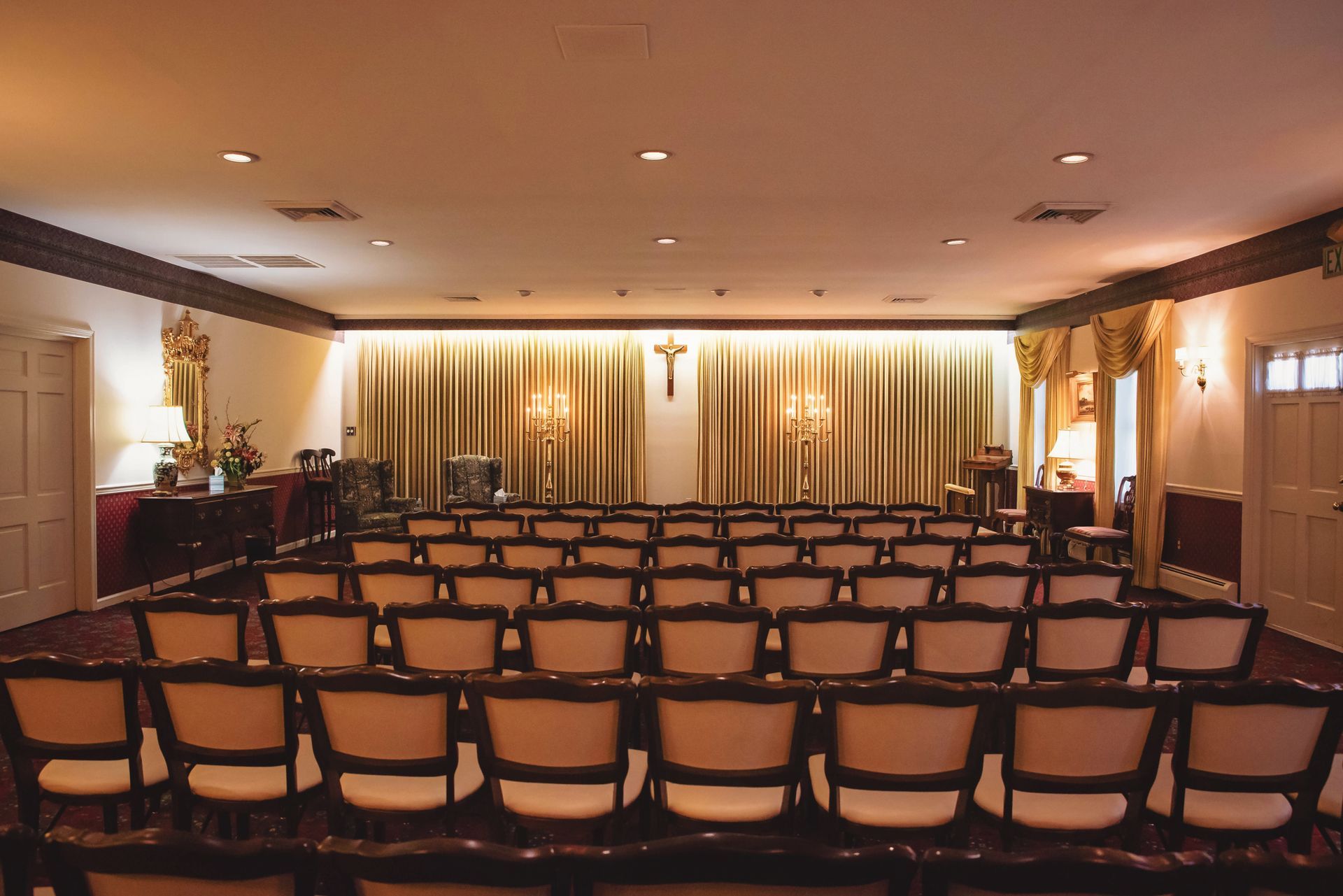 A carpeted room with chairs facing a fireplace, a podium, and soft lighting, likely a funeral home or event space.