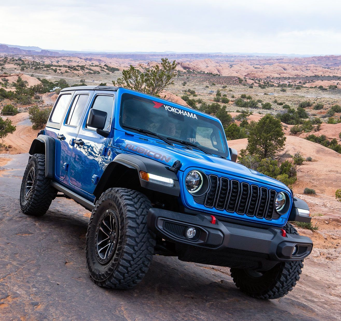 Blue Jeep off-roading on a desert trail with rocky hills in the background