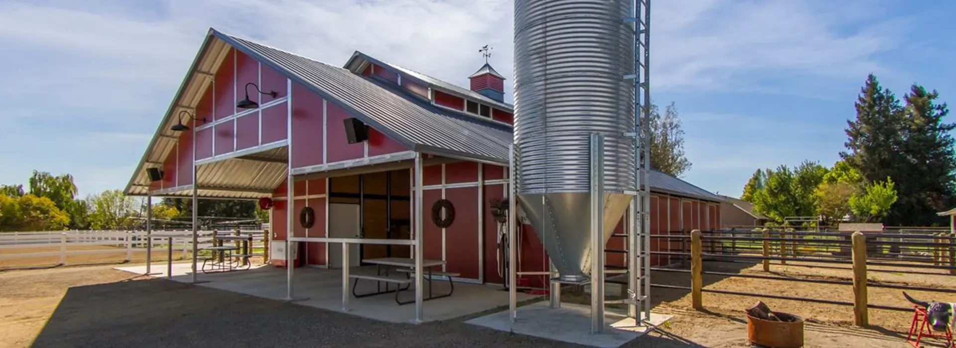 A red barn with a metal silo in front of it.