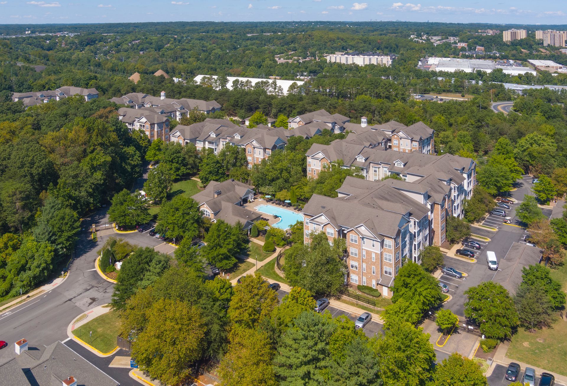 Aerial view of apartment buildings with a pool surrounded by trees.