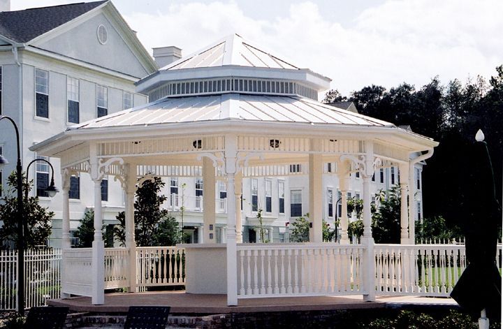 A white gazebo with a metal roof sits in front of a white house