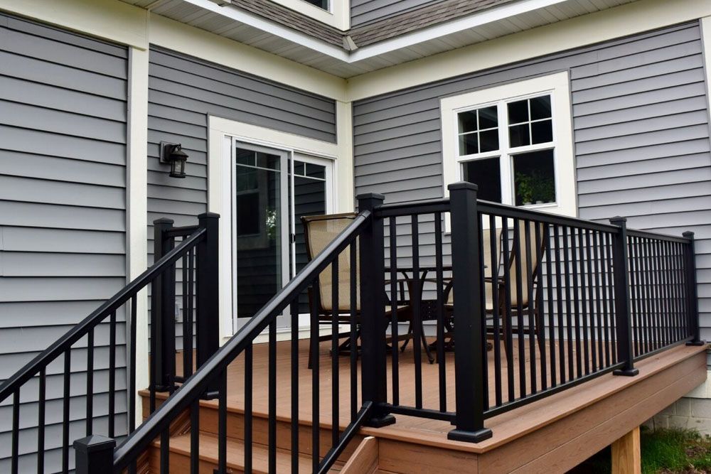 There is a deck with a table and chairs on it in front of a house.