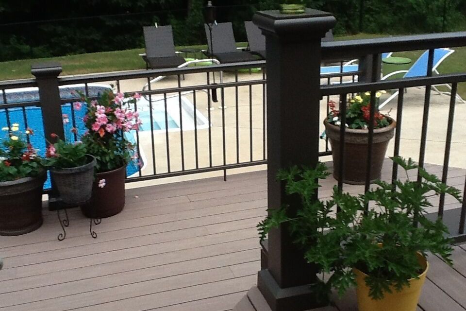 A deck with potted plants and a pool in the background