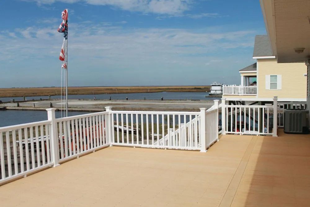 Empty waterfront deck with white railing and a flagpole under a blue sky