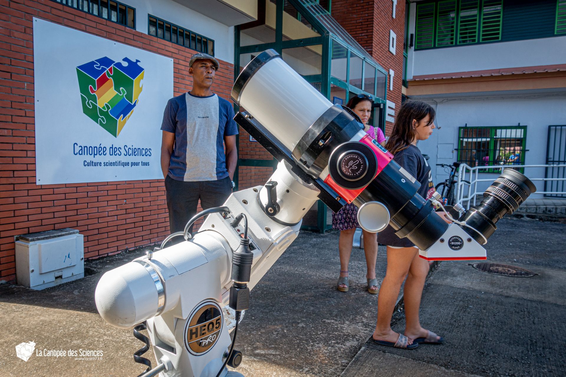 Un groupe de personnes regarde à travers un télescope devant un bâtiment.
