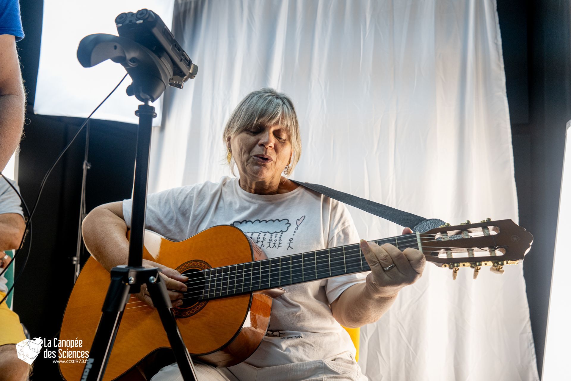 Une femme joue de la guitare devant un rideau blanc.