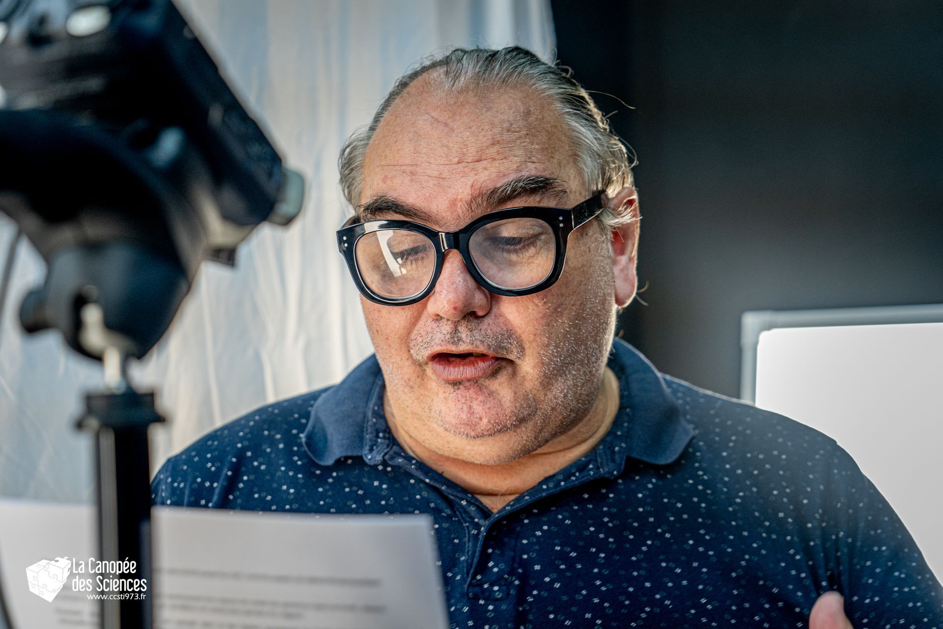 Un homme portant des lunettes lit un morceau de papier devant une caméra.