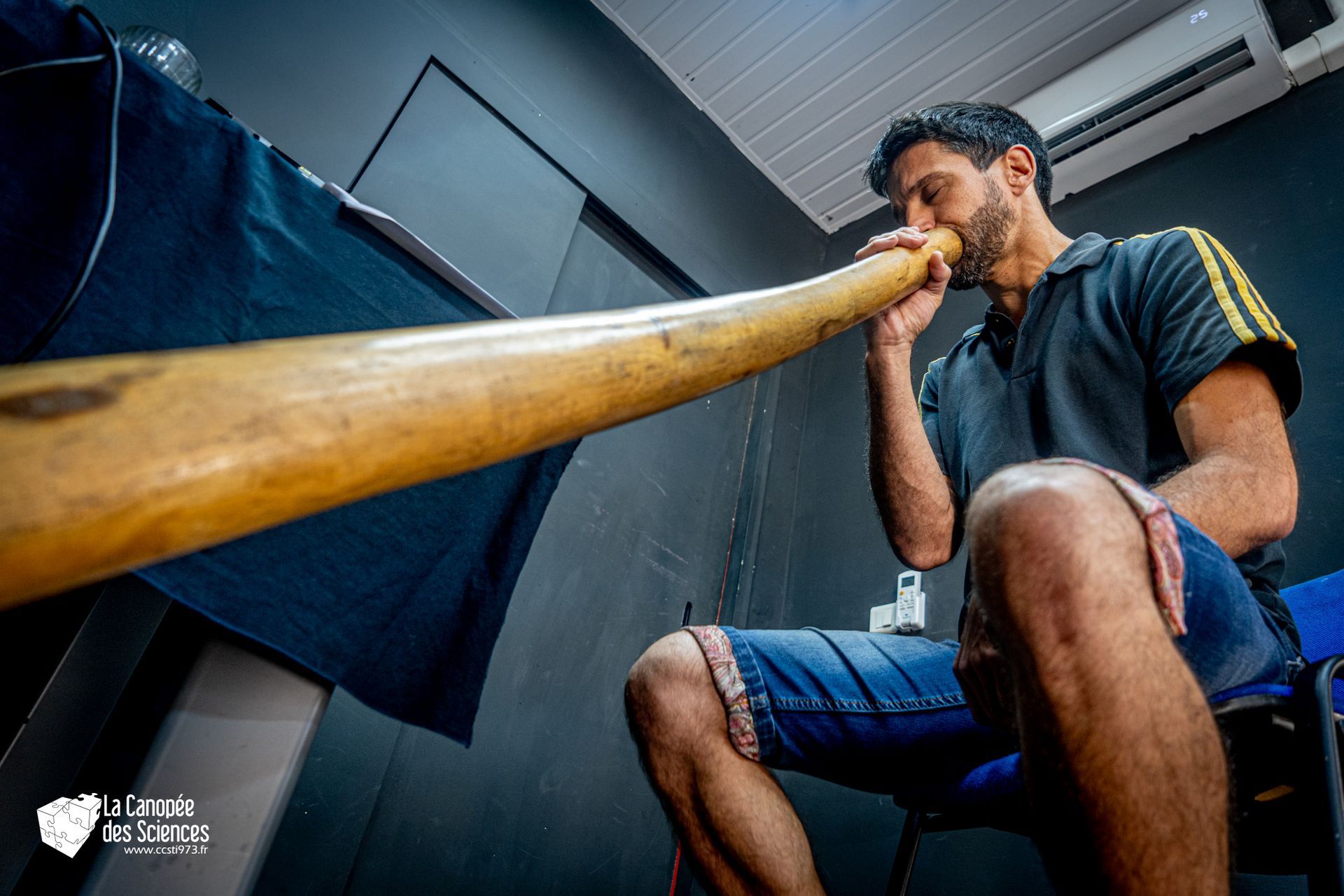 Un homme est assis sur une chaise et joue d'un long instrument en bois.