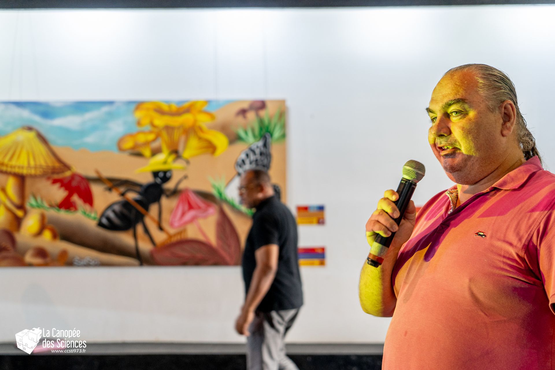 Un homme tient un microphone devant un tableau représentant une fourmi.