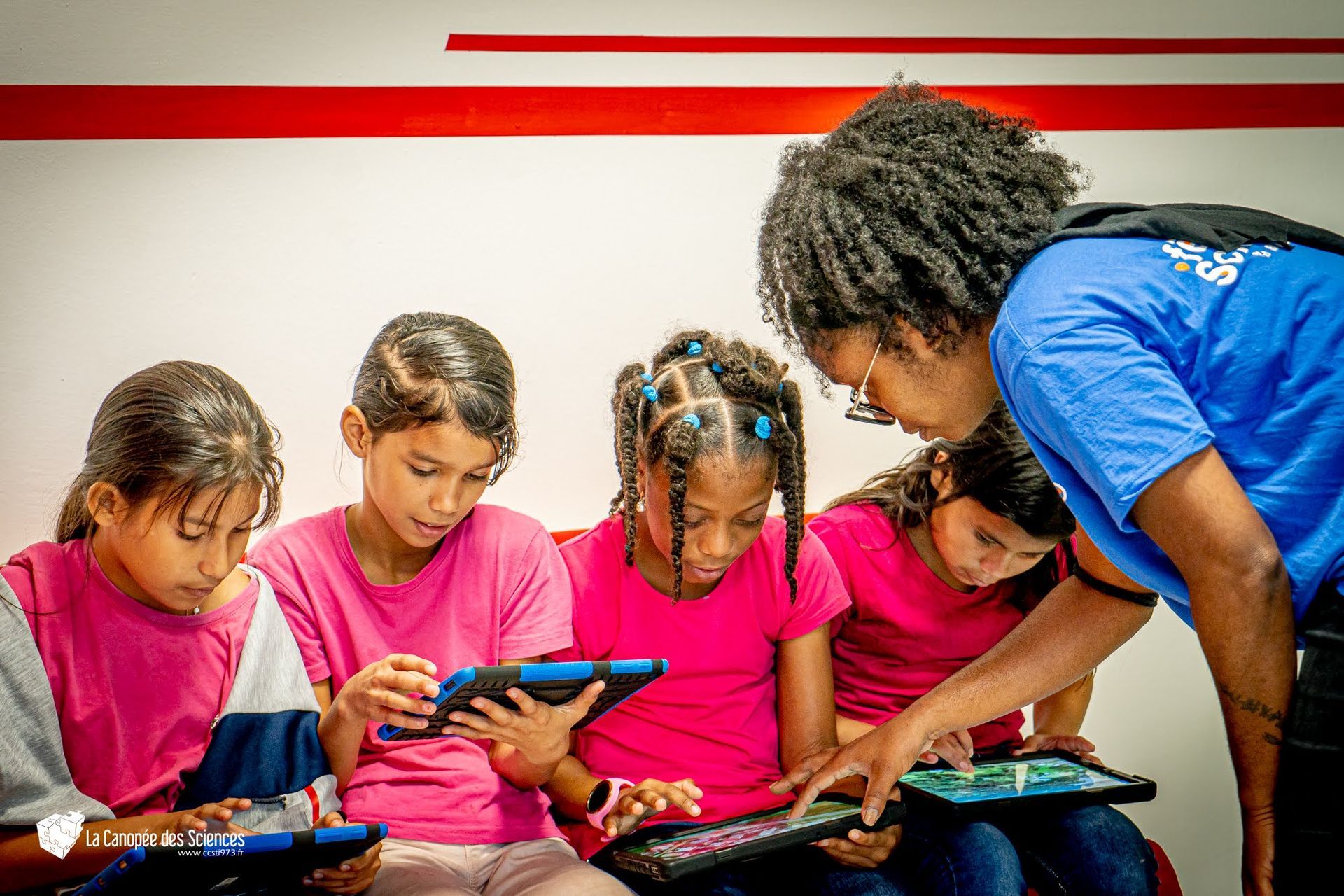 Une femme enseigne à un groupe de jeunes filles comment utiliser une tablette.