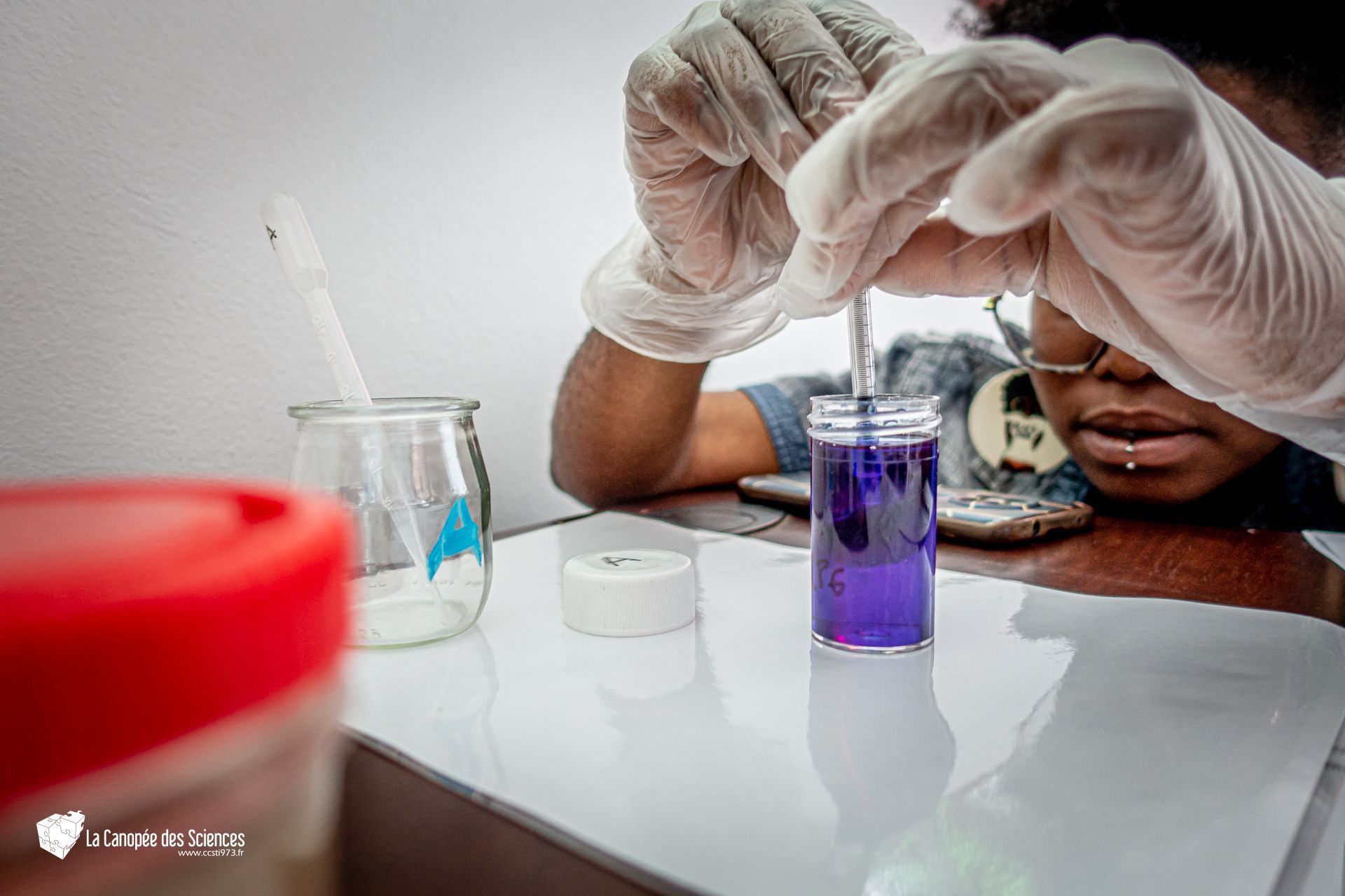Une personne portant des gants tient un liquide violet dans un bocal.