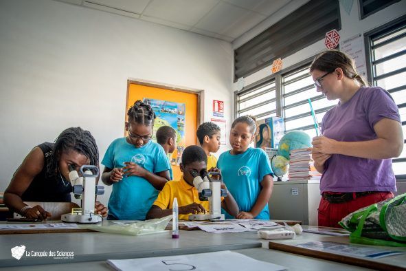 Un groupe d'enfants regardent à travers des microscopes dans une salle de classe.