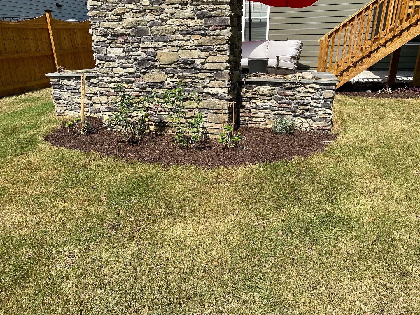 Stone chimney and raised flowerbed against a yellowed lawn, with a wooden deck in the background.