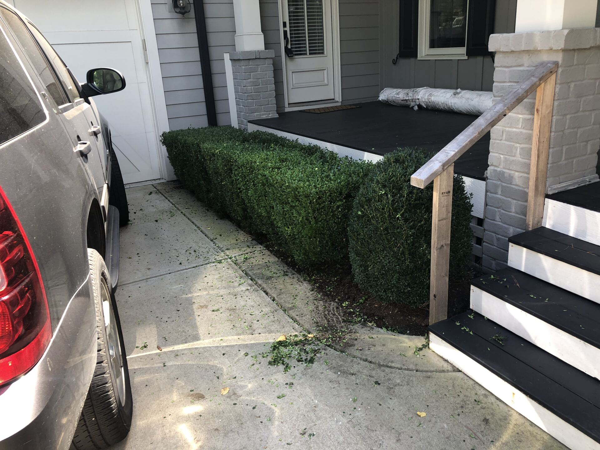 A trimmed hedge next to a porch with steps, a car parked nearby.