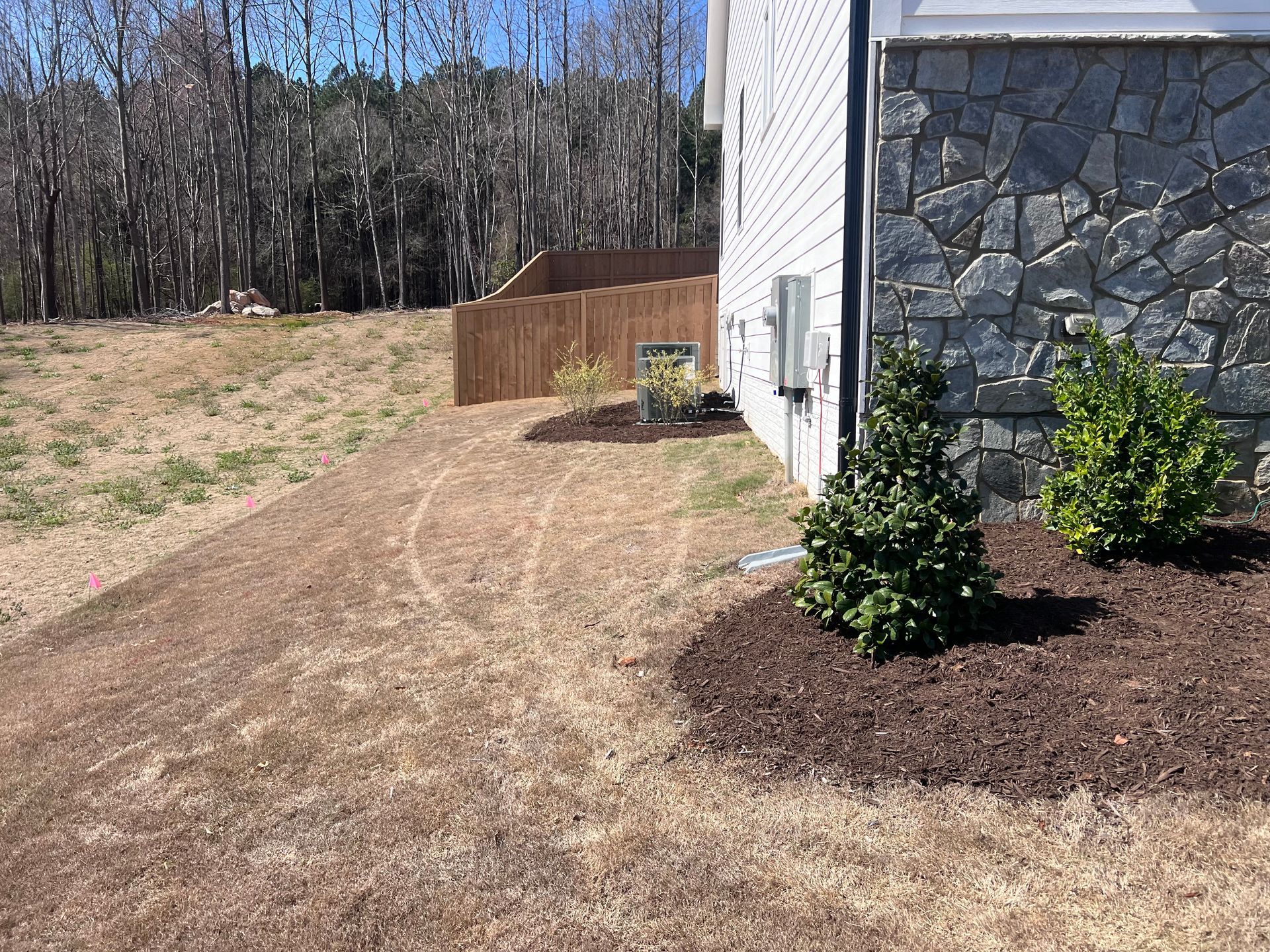 A house exterior with stone veneer and landscaping, including mulch, shrubs, and a sloped, grassy yard.