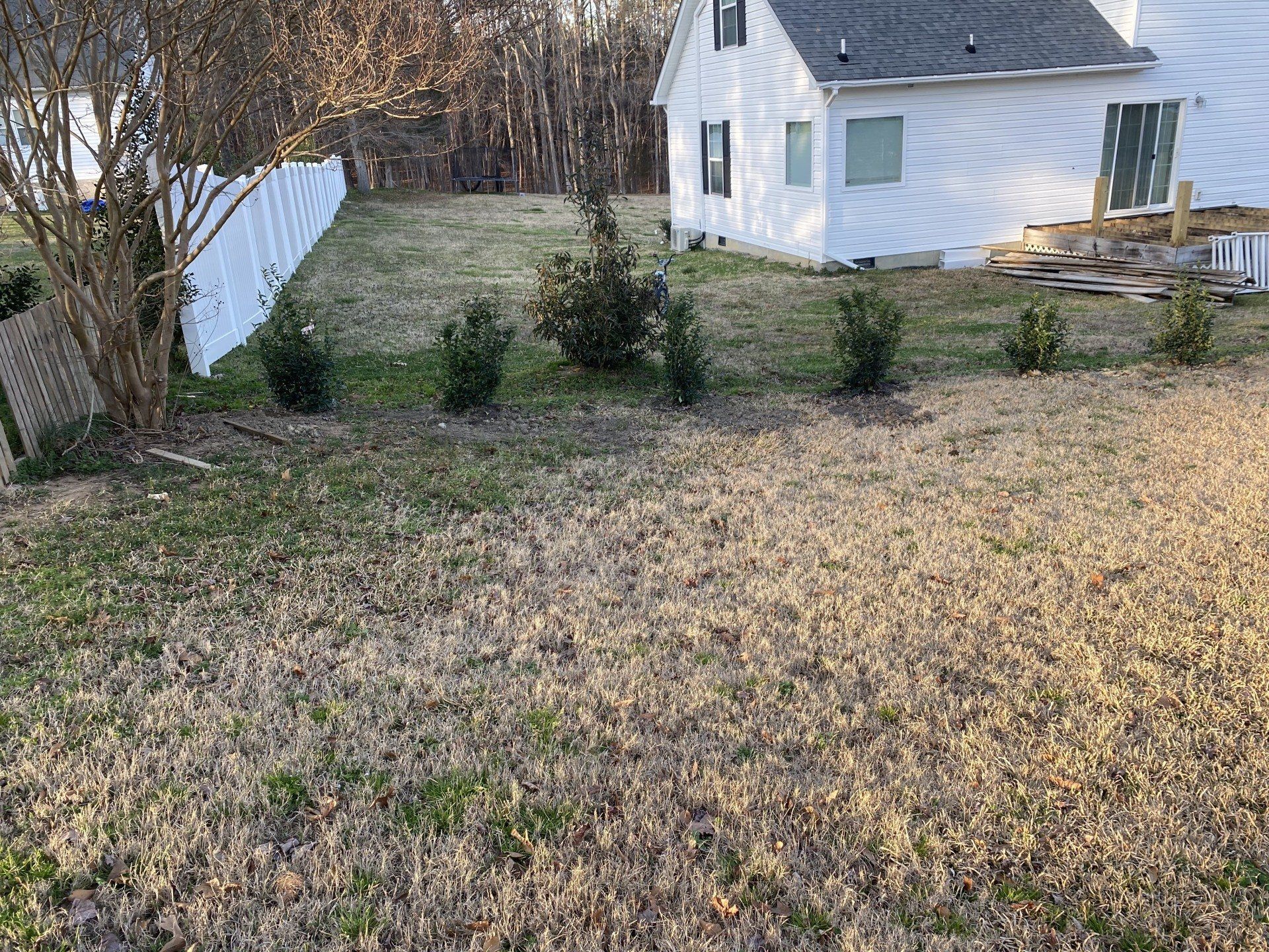 Backyard with a white fence, green shrubs, and a white house.