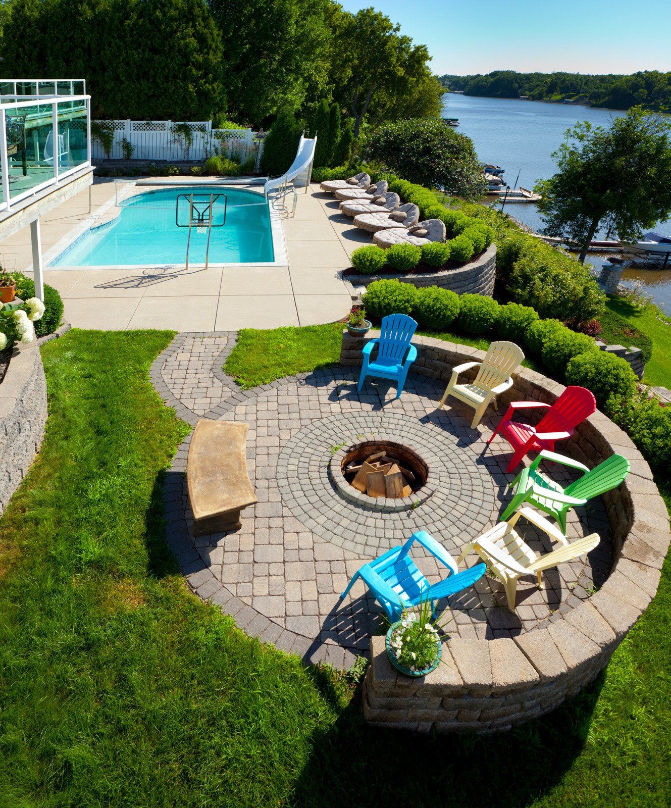 Outdoor patio with fire pit and colorful Adirondack chairs overlooking a pool and waterfront.