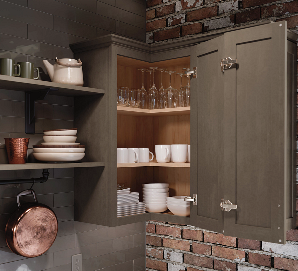 Open kitchen cabinet with glassware, mugs, and stacked dishes against a brick wall