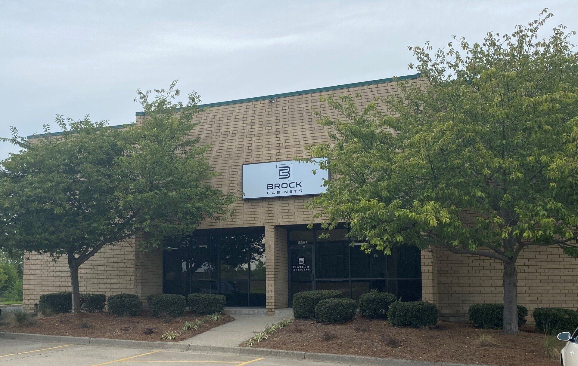 Front entrance of a beige brick building with trees and a centered sign above the doors.