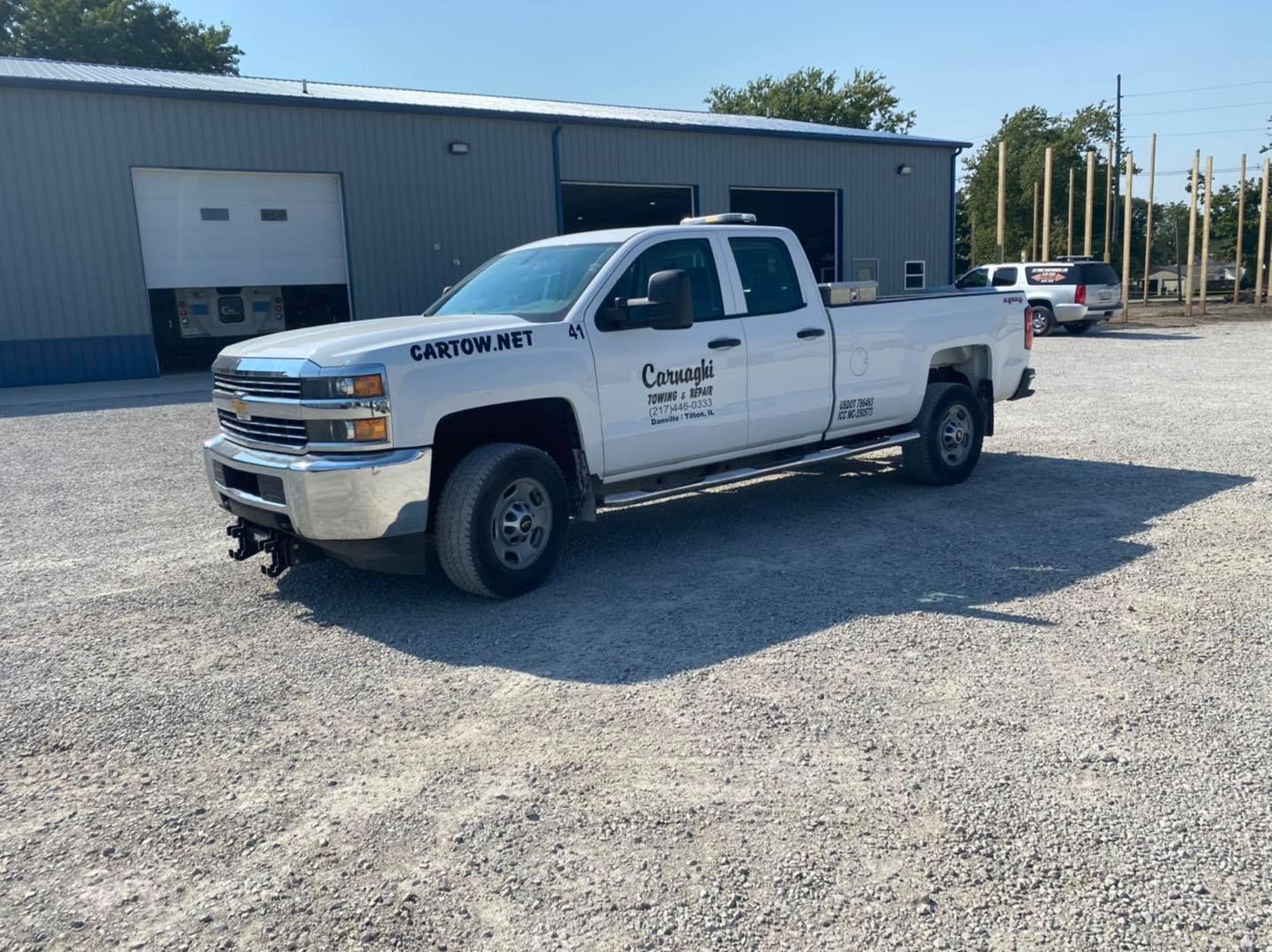 A white truck is parked in a gravel lot in front of a building.