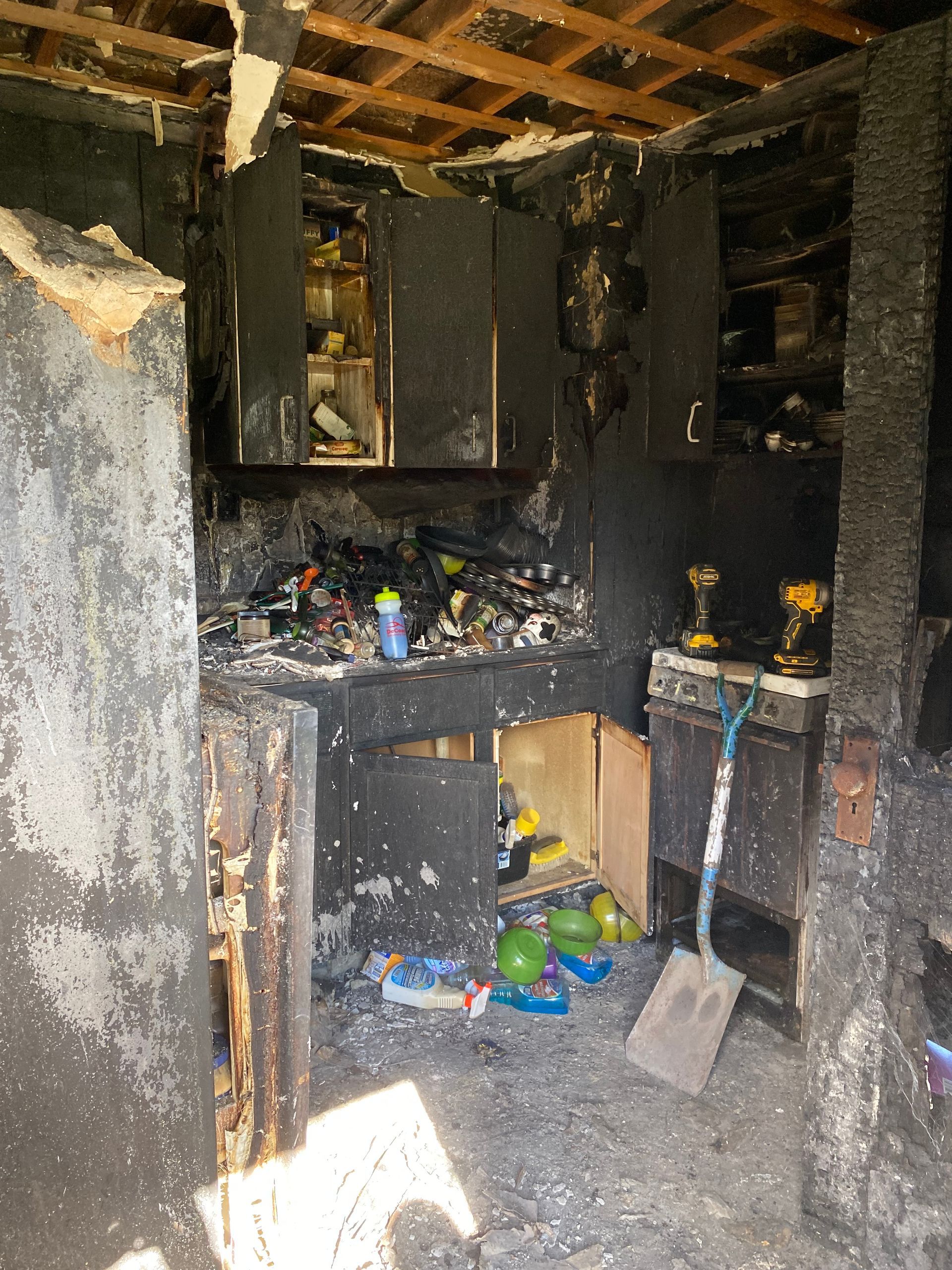 Burned kitchen interior with charred cabinets, soot-covered walls, and scattered debris