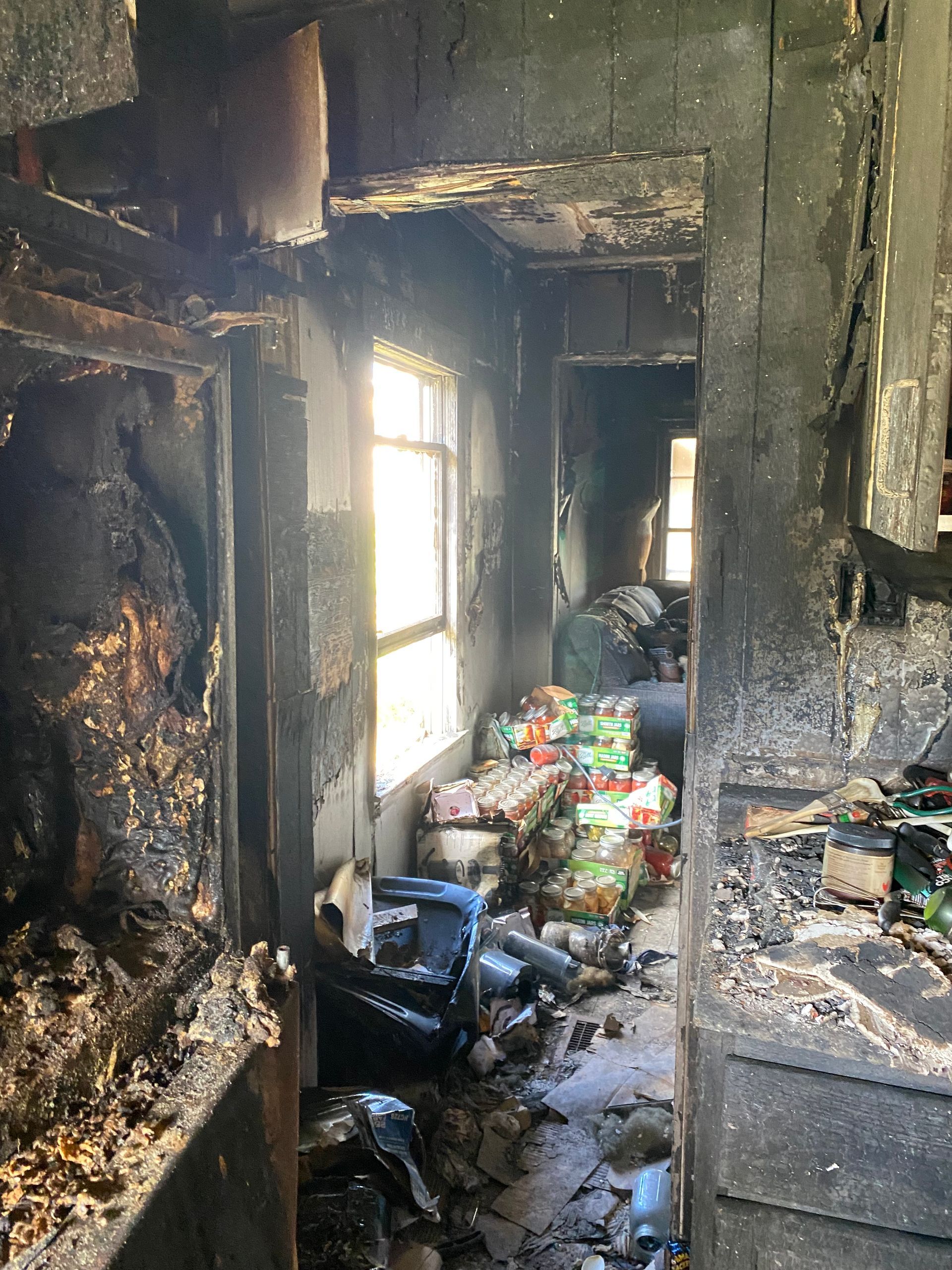 Charred hallway in a burned building, with debris on the floor and light through a window.