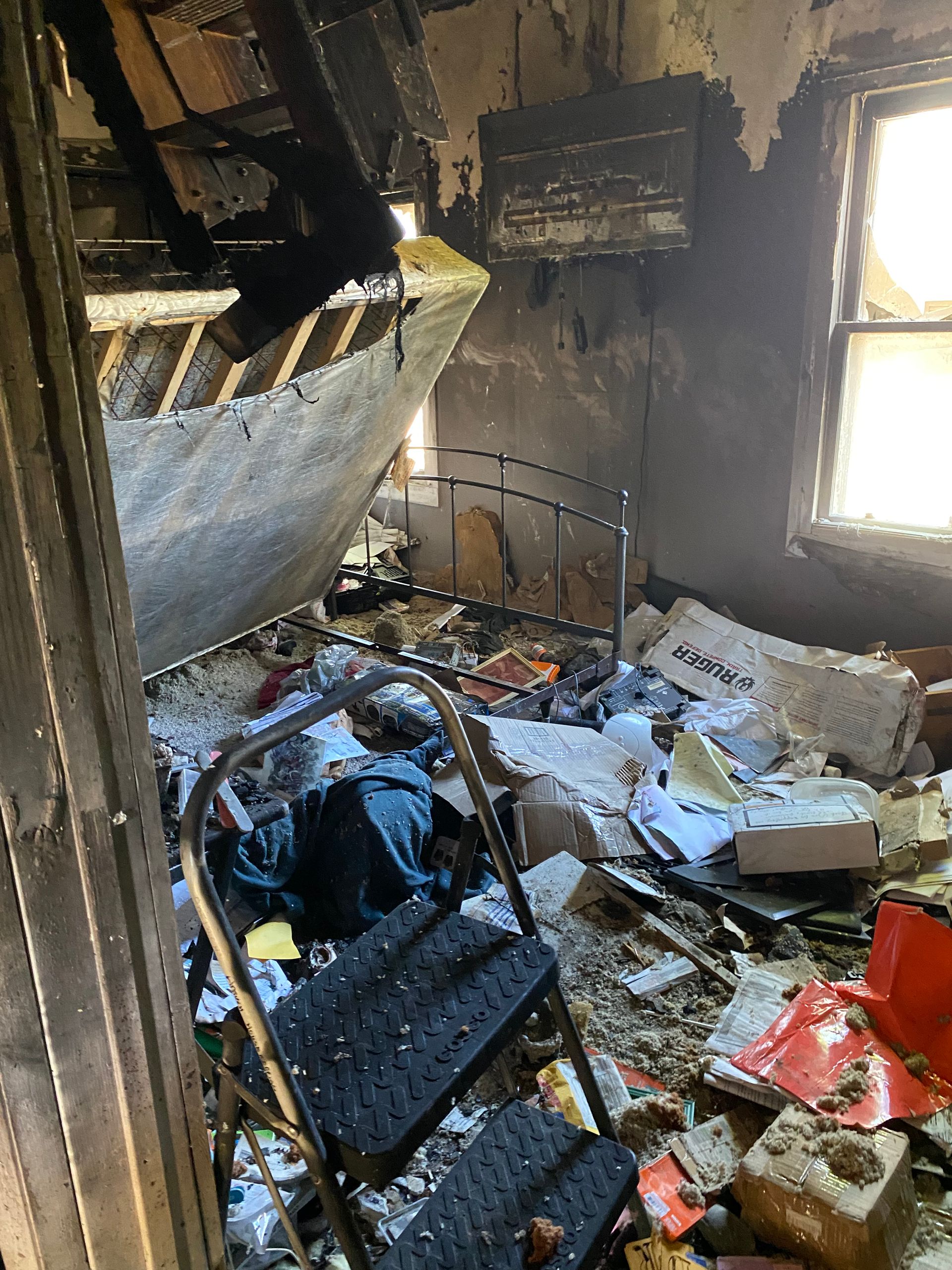 Fire-damaged room with debris, charred walls, and a broken window letting in daylight