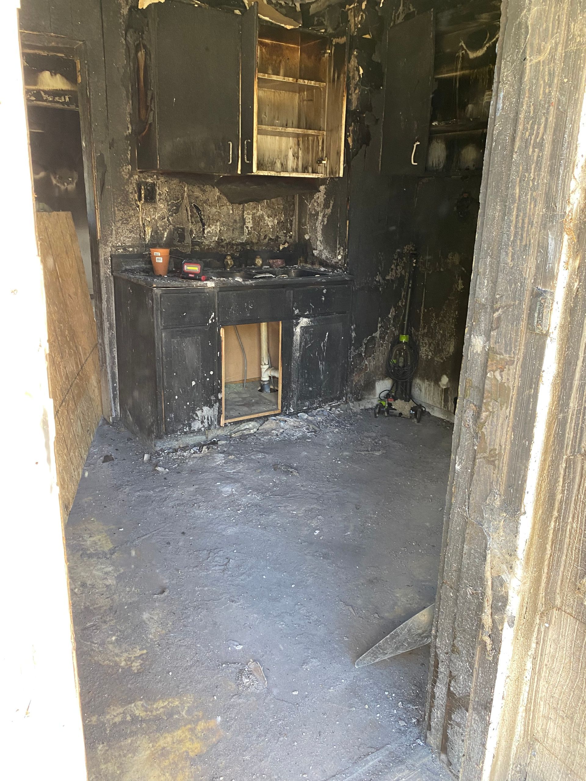 Fire-damaged kitchen interior with blackened walls, cabinets, and debris on the floor
