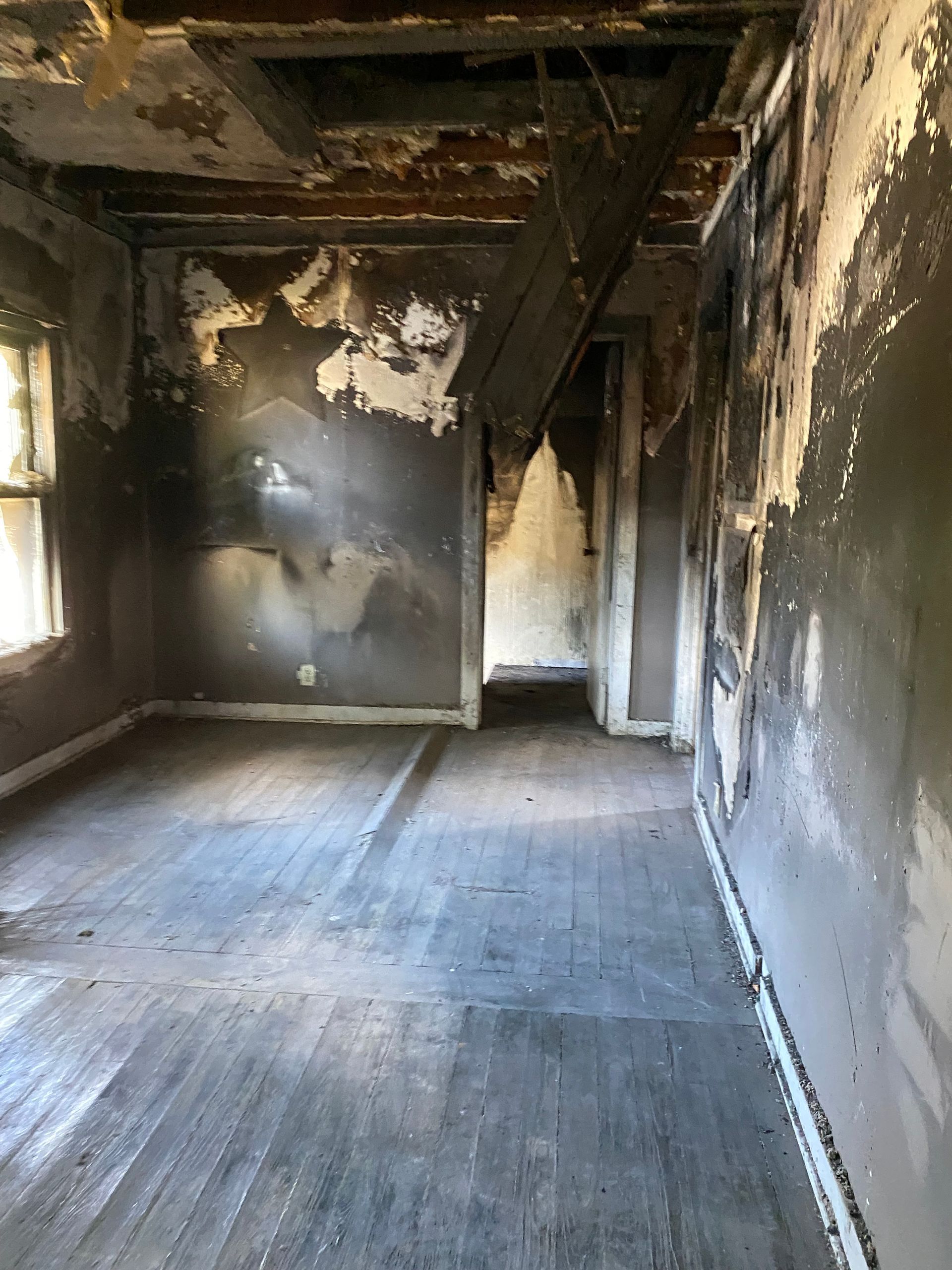 Severely fire-damaged empty room with blackened walls, charred ceiling, and a bare floor.