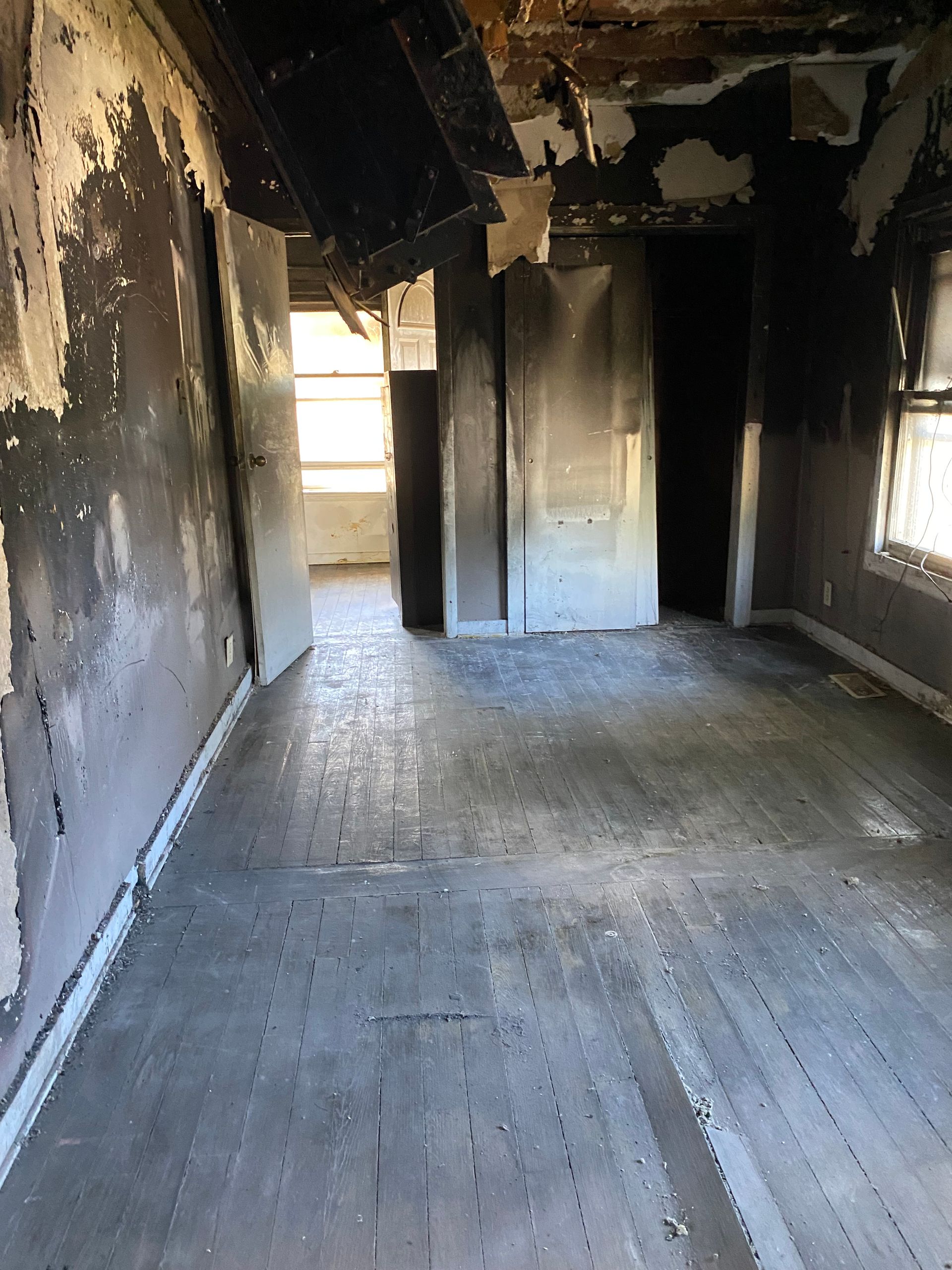 Burned-out empty room with charred walls, damaged ceiling, and a bright window at the far end