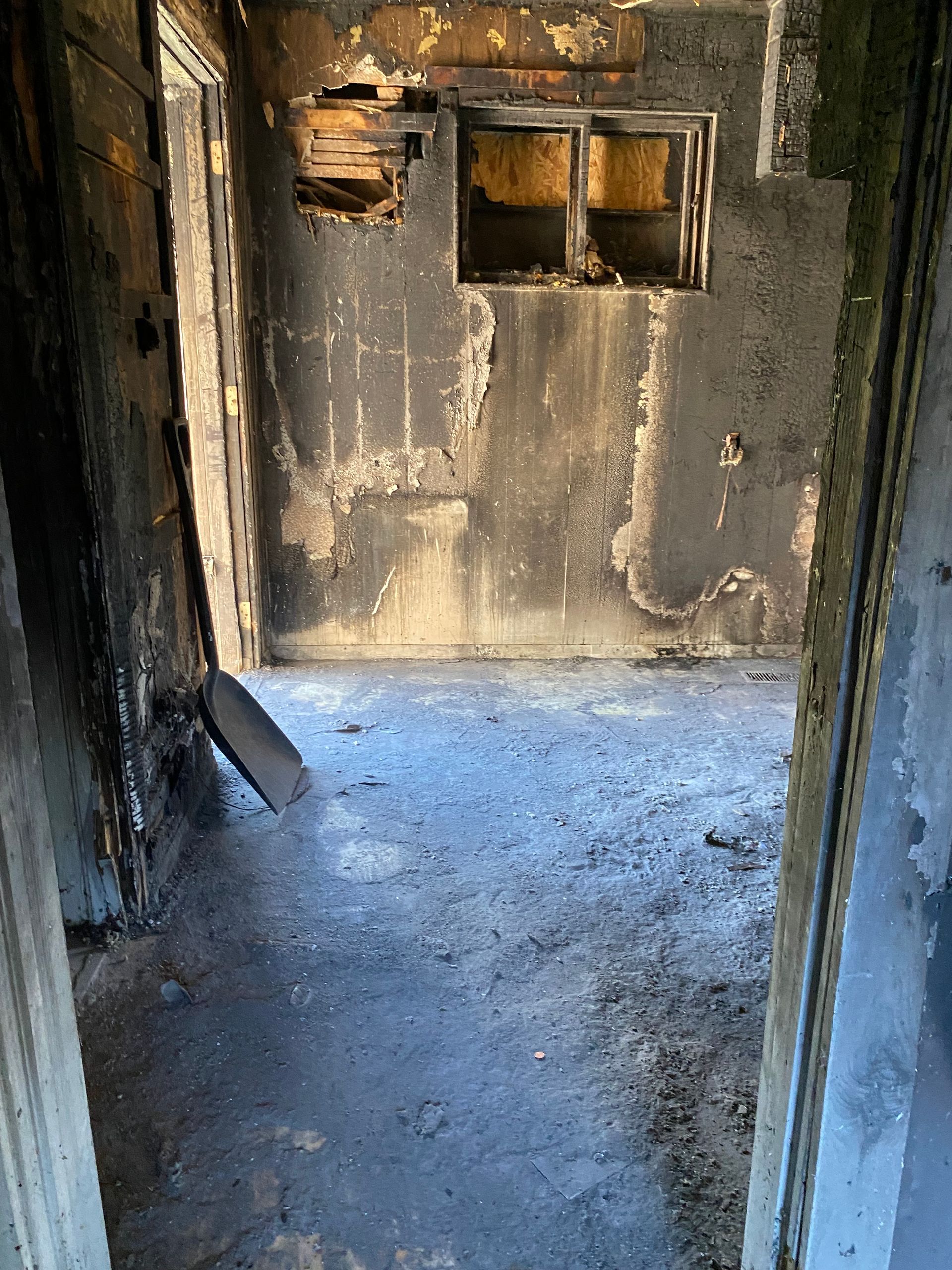Soot-stained doorway opening into a fire-damaged room with charred walls and debris on the floor