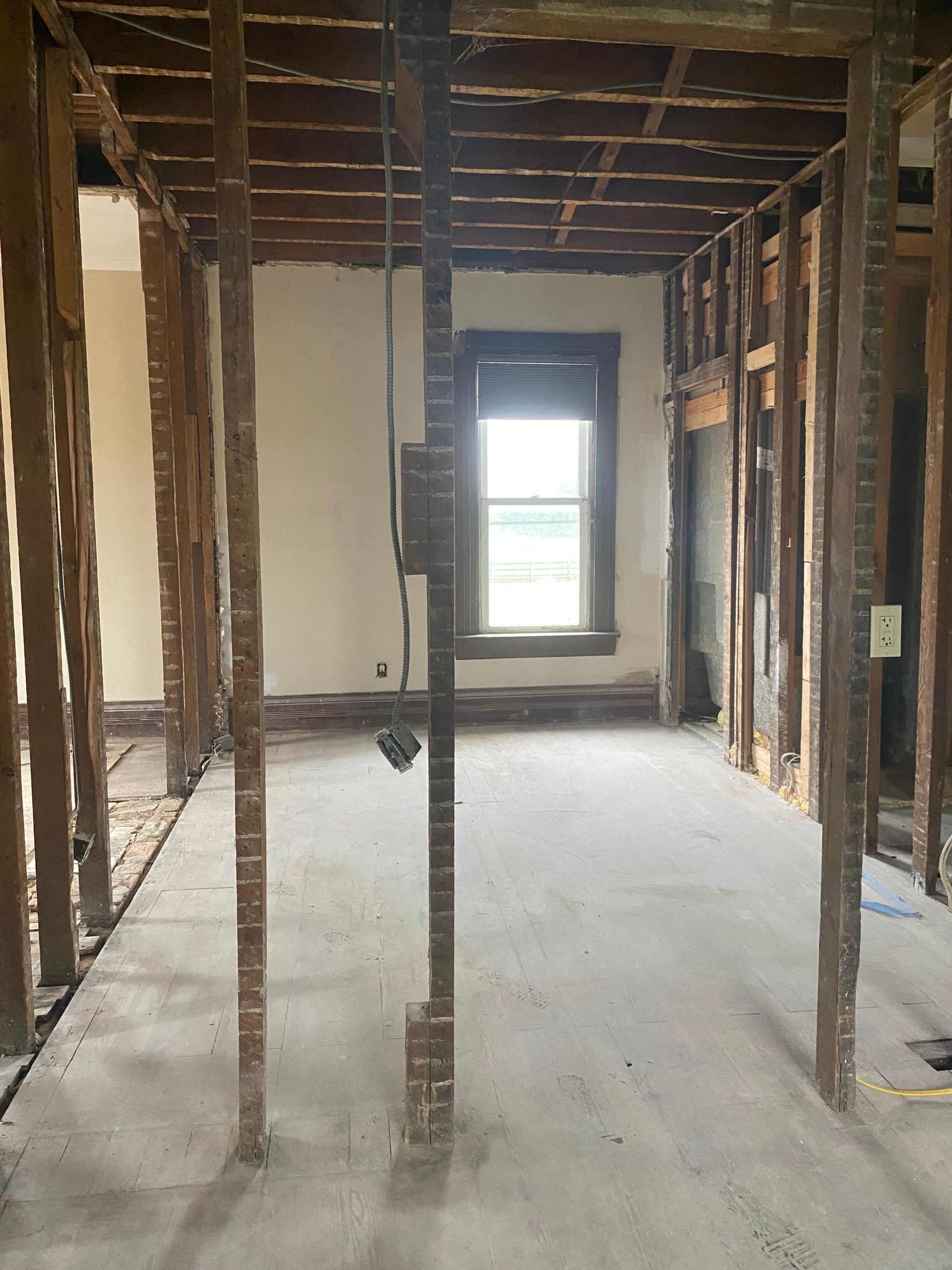 Exposed interior room under renovation with bare studs, unfinished walls, and a window at the far end.