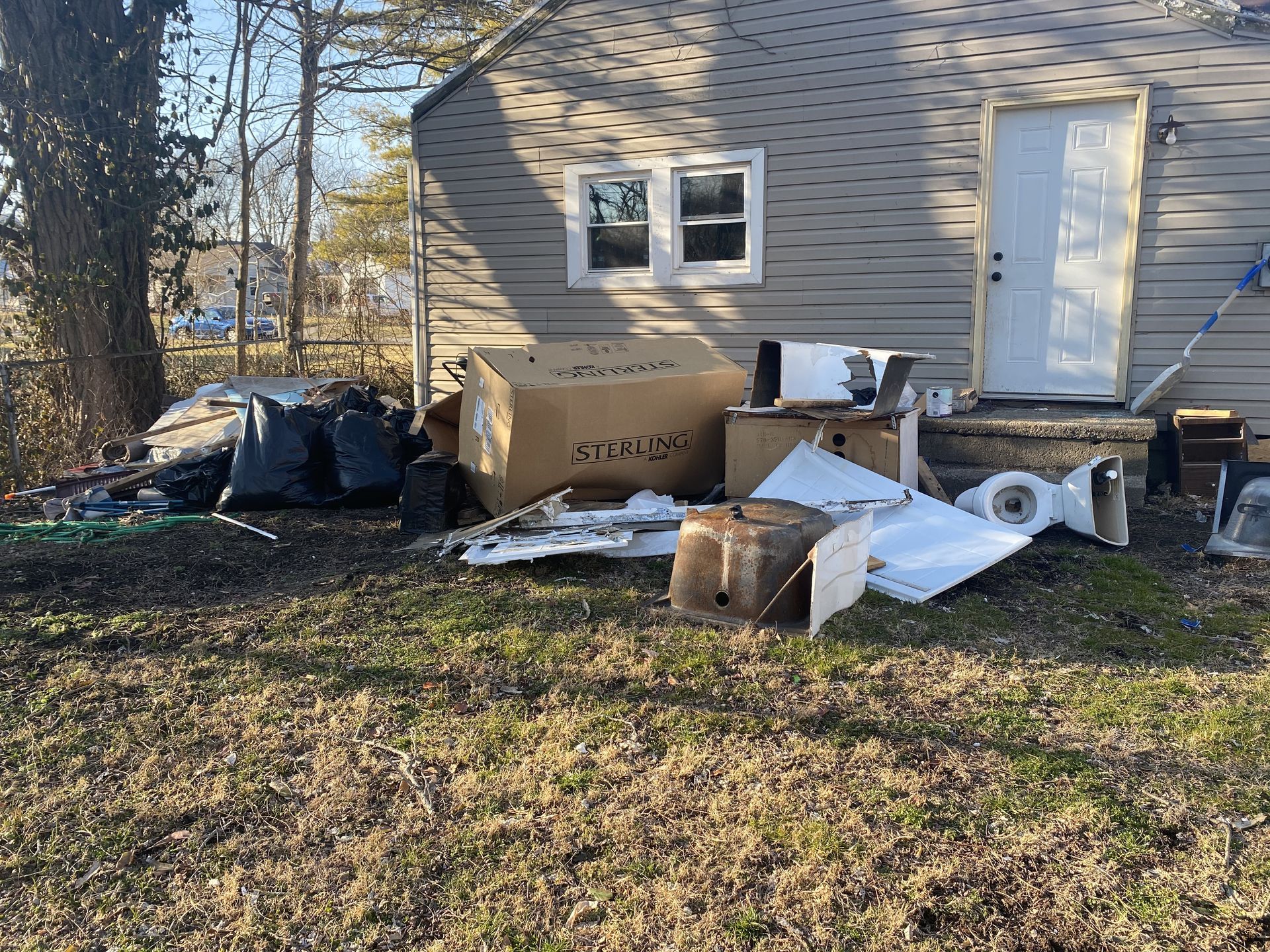 Debris and discarded furniture piled beside a house in a yard.