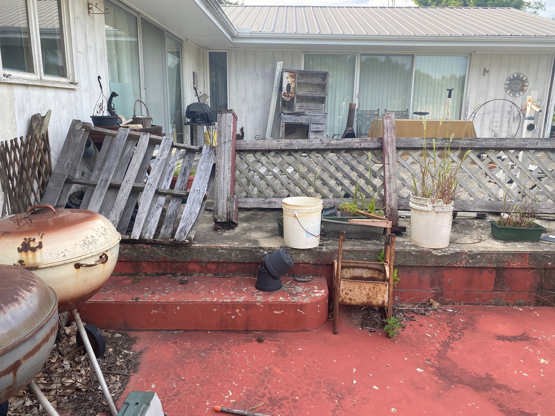 Weathered backyard patio with red steps, lattice fence, potted plants, and stacked wooden pallets.