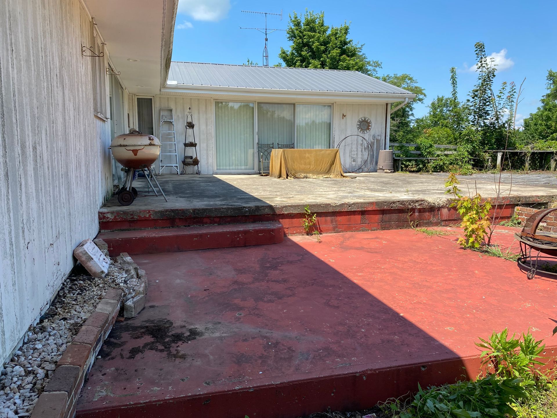 Red patio and concrete steps leading to a white house with a covered porch and potted plants.