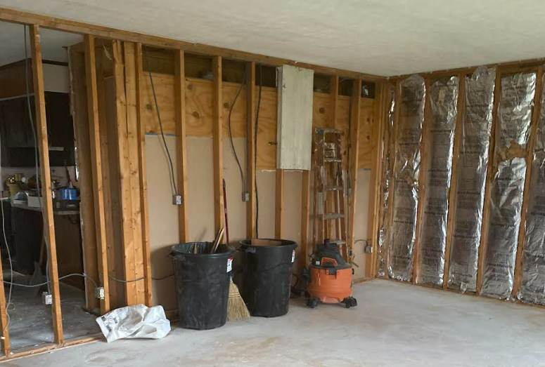 Unfinished basement with exposed studs, trash bins, and an orange shop vacuum on the concrete floor.