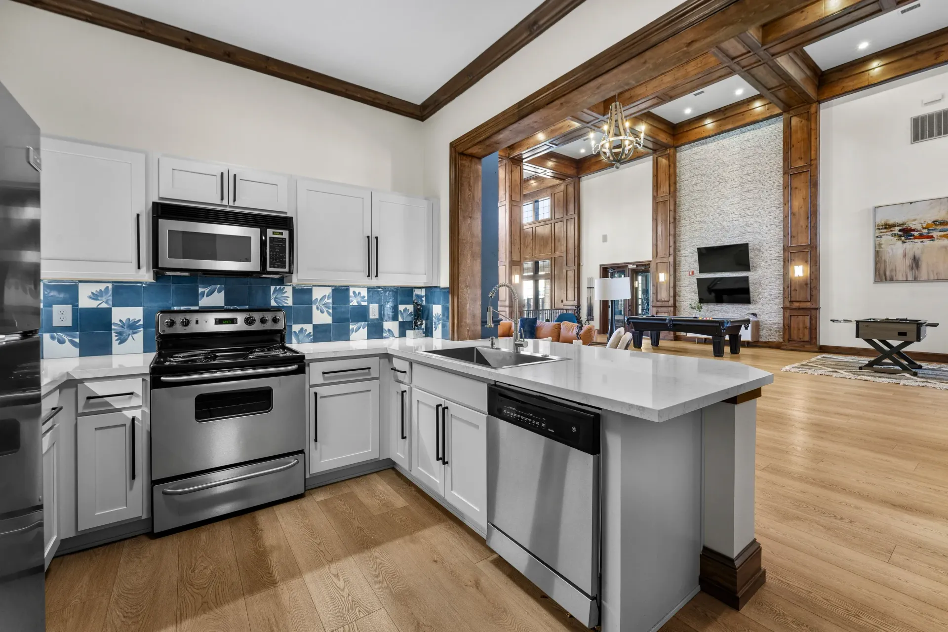Open-concept kitchen with stainless steel appliances, white cabinets, and a blue tile backsplash.