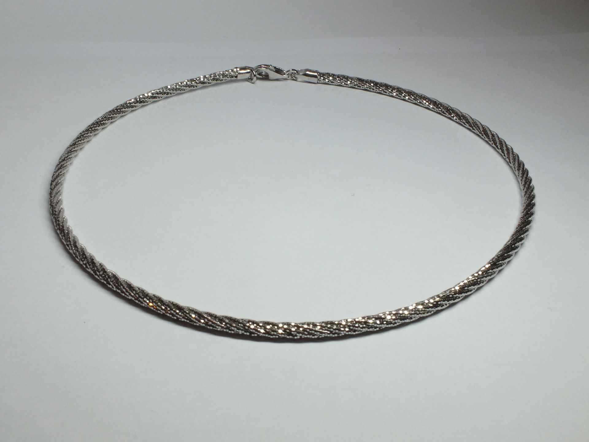 Una collana d'argento è appoggiata su una superficie bianca