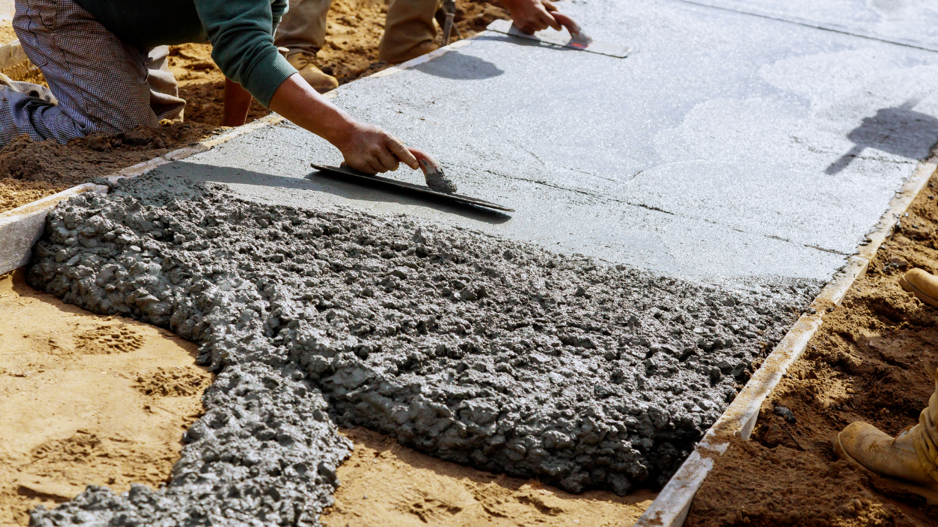 Workers spreading fresh concrete on a construction site with a trowel