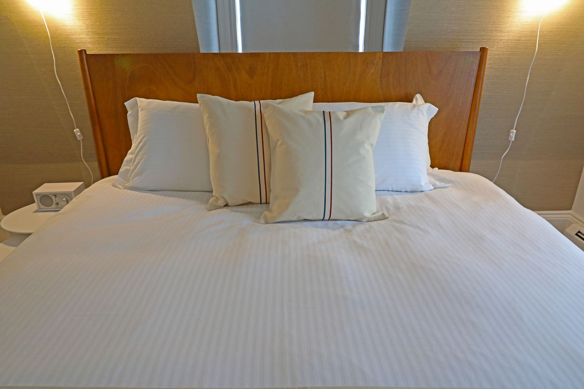 A neatly made bed with white striped bedding, two plain white pillows, and two accent pillows with vertical stripes.
