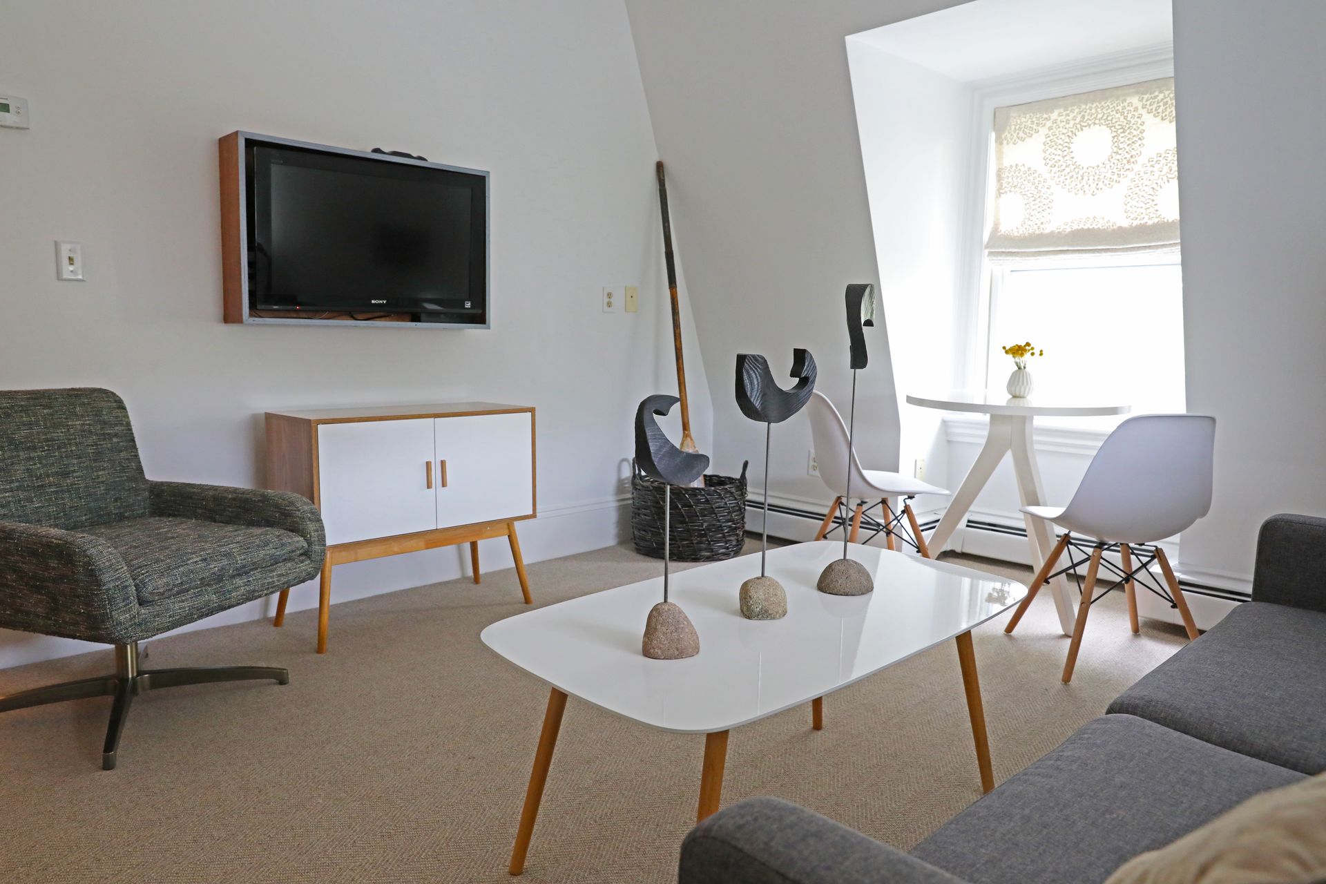 A bright, modern living room featuring a grey armchair, a sofa, a coffee table with sculptures, and a dining nook.
