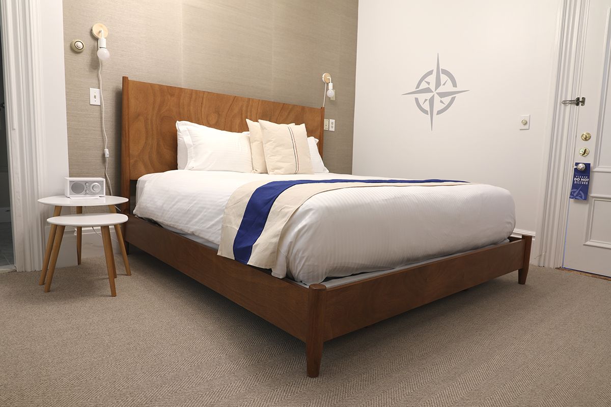 A hotel room features a wooden bed with white bedding, a blue runner, and a compass rose wall decal above it.