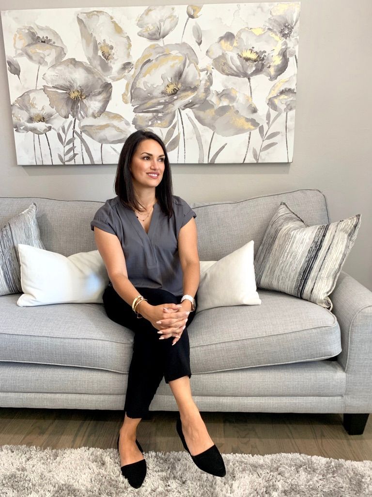Woman sitting on a gray sofa in a living room with a floral painting above it.