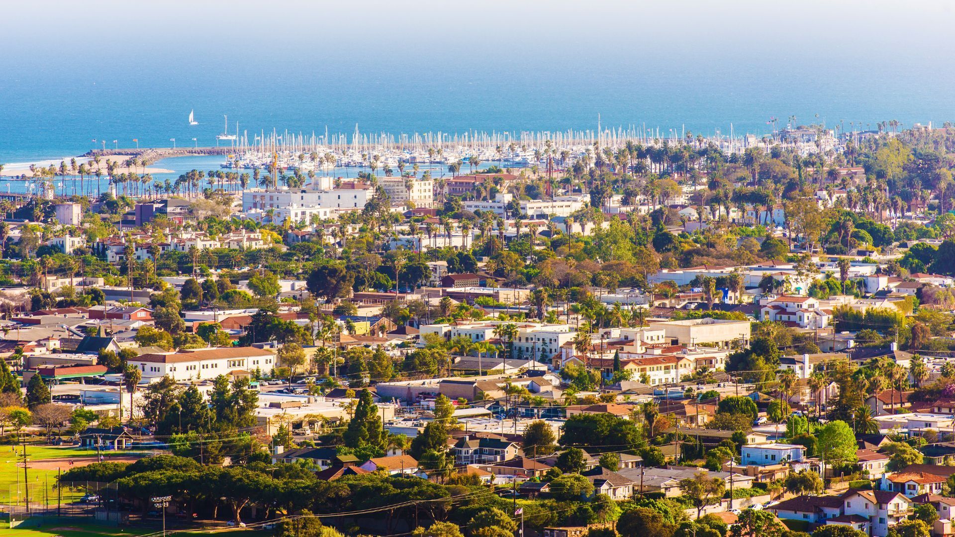 Aerial view of a coastal city with dense buildings, green neighborhoods, and ocean in the background